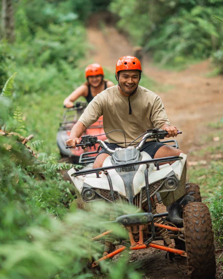 Driver and passenger sharing one quad bike, both in helmets, on a narrow jungle trail