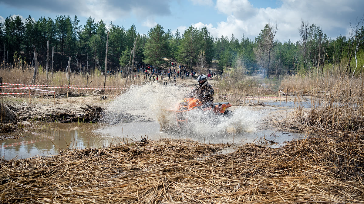 A quad bike throwing up a wall of spray as it powers through a flooded section of trail