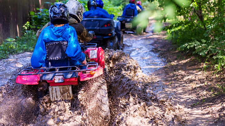 Group of quad riders on a muddy jungle trail seen from behind
