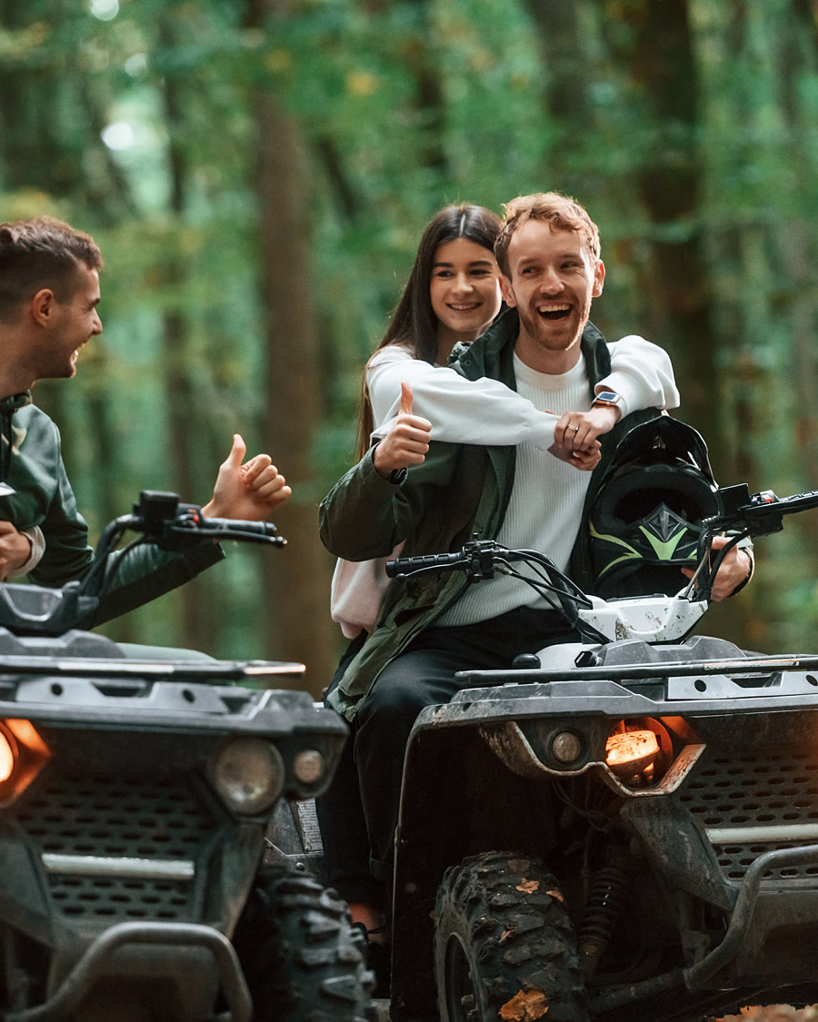 Four people sharing two off-road vehicles on a forest track, laughing
