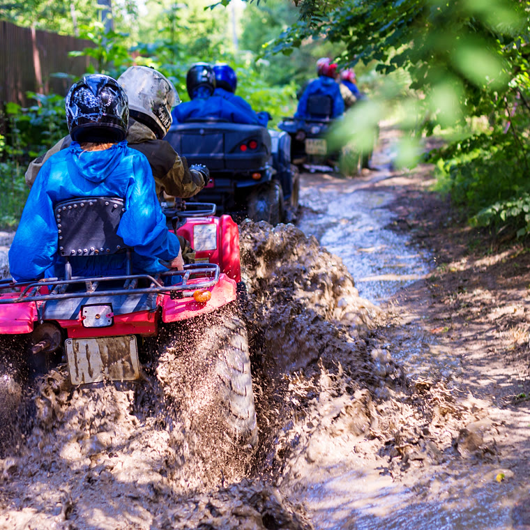 Riders on quad bikes splashing through deep mud on a jungle trail