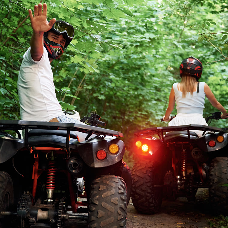 Two quad riders on a narrow trail between dense green foliage