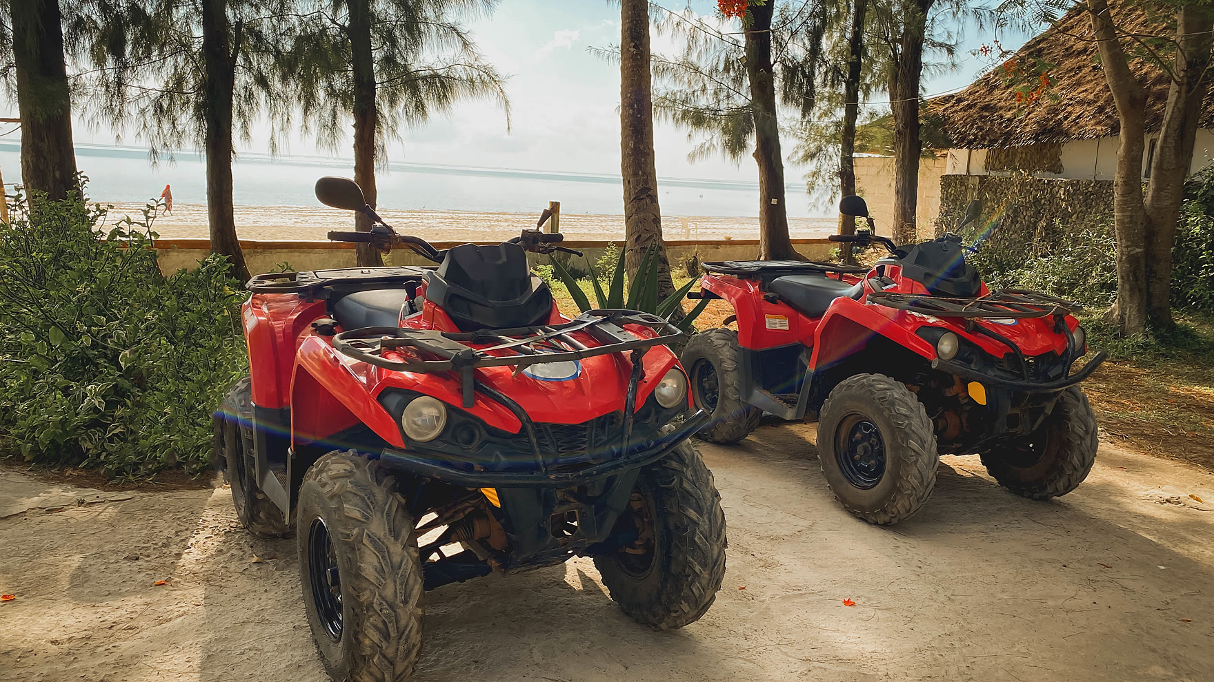 Two red quad bikes parked side by side on a sandy track under palm trees before a Pattaya jungle tour sets off