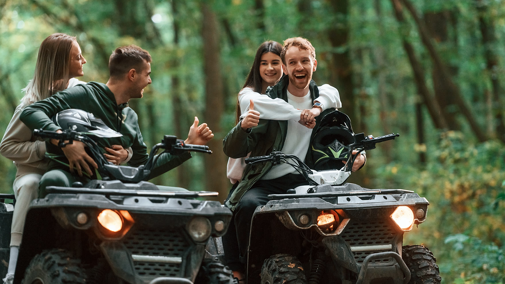 Two couples laughing together on their quad bikes on a forest track at the end of a ride