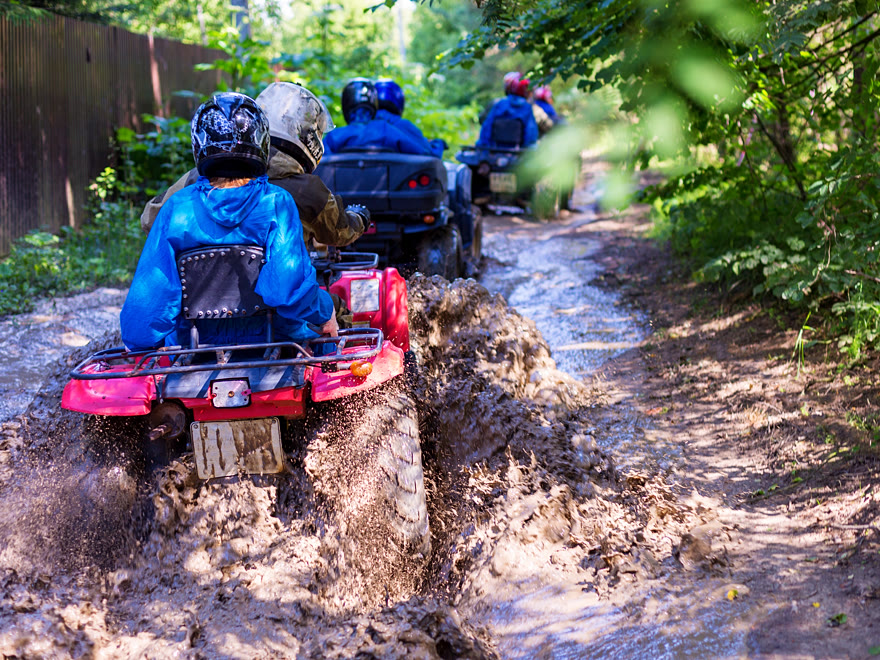 Group of quad riders throwing up mud on a deeply rutted jungle trail