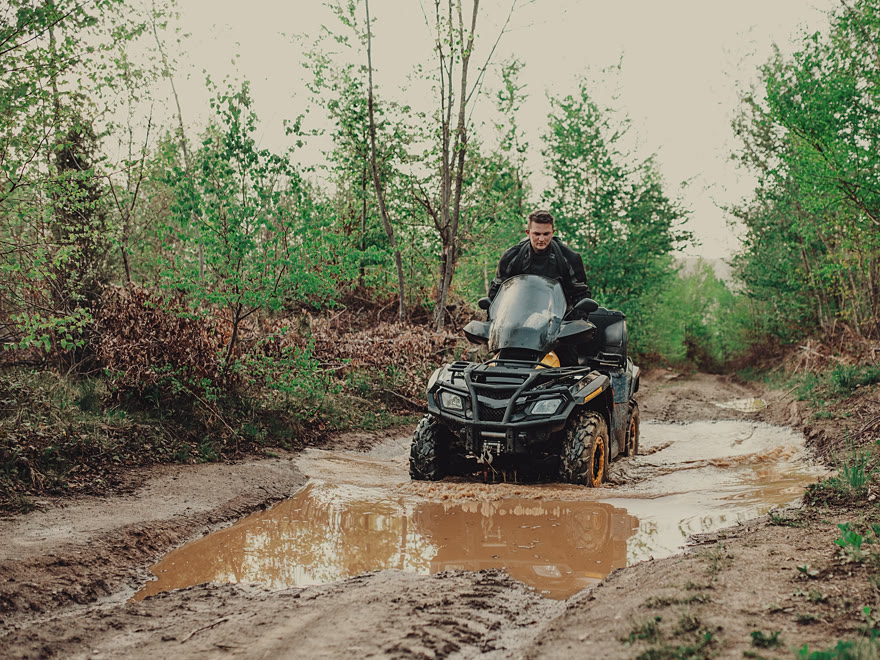 Rider in a white helmet on a quad bike crossing a muddy forest track