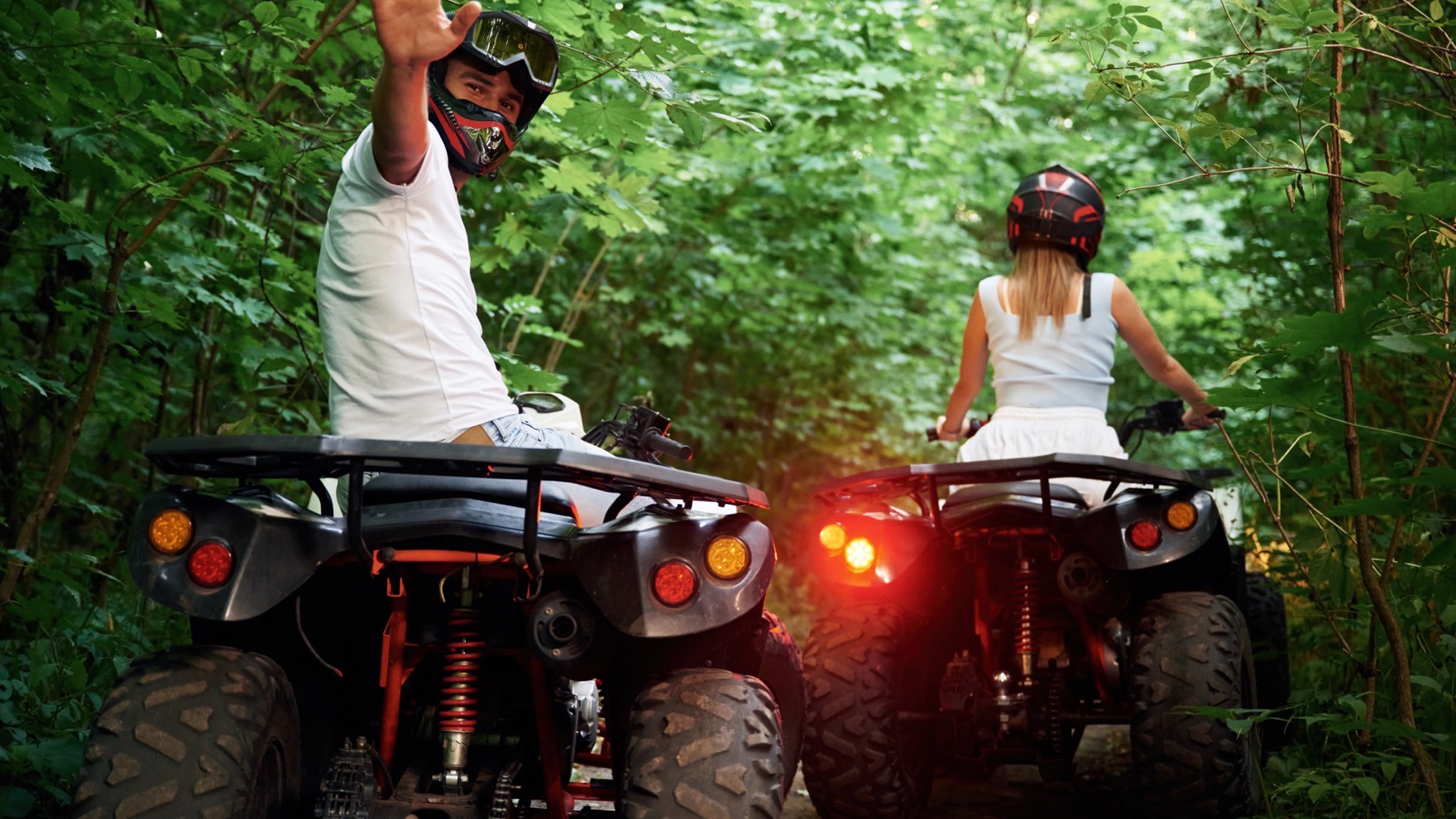 A couple riding quad bikes side by side on a quiet forest track on a private VIP tour