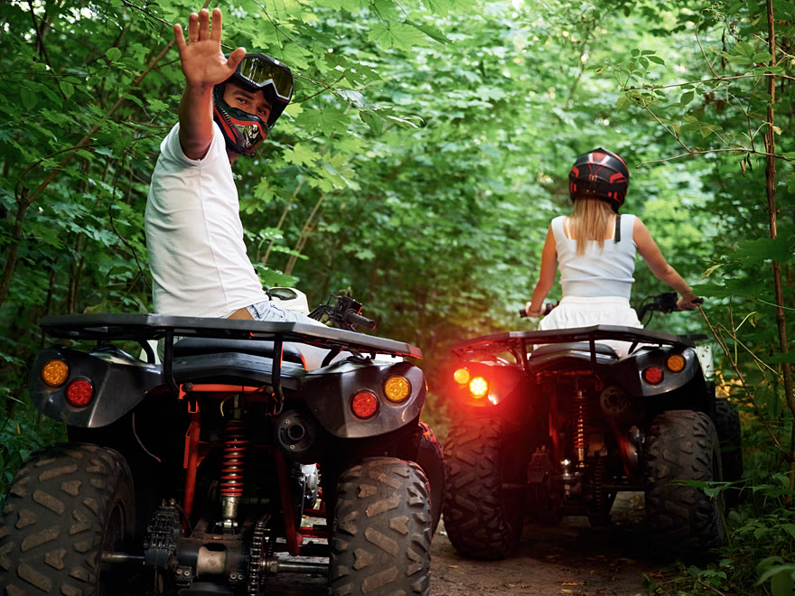 Two riders on quad bikes waving on a narrow jungle trail on a private tour
